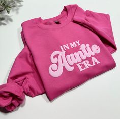 a pink t - shirt with the words in my annie era printed on it, sitting next to a potted plant