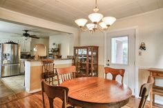 a dining room table and chairs in front of an open kitchen area with a refrigerator