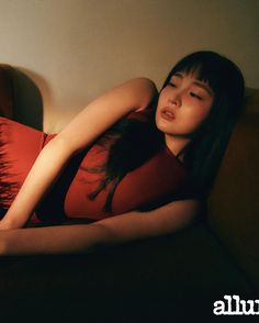 a woman laying on top of a brown couch next to a red pillow with her eyes closed