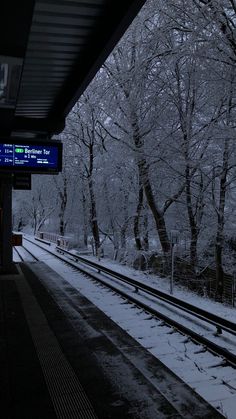 a train station with snow on the ground and trees covered in snow, at night