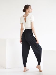 a woman standing in front of a white wall wearing black pants and a t - shirt