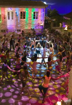 a large group of people doing various activities in front of a building with colored lights