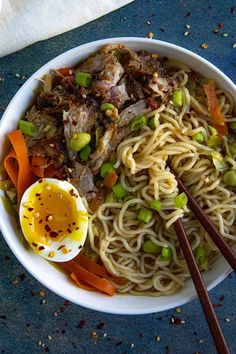 a bowl filled with noodles, meat and veggies next to chopsticks