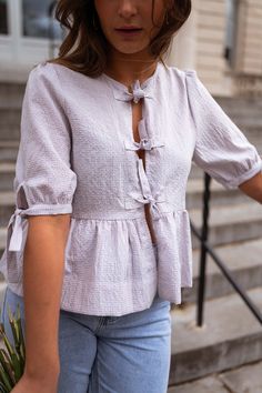 Lilac gingham patterned slight-balloon short sleeve blouse that features a cute bow to tie in the front, as well as bow detailing on the sleeves. This blouse has a flowy-slightly loose fit and dies not offer lining. The perfect unique and trendy spring-summer wardrobe staple. Our models also wear the White Baptiste Jeans and the Light Blue Maddie Jeans. Sizes: S / M / L S: Length 20.87 in - Width 18.11 in M: Length 21.26 in - Width 18.90 in L: Length 21.65 in - Width 19.69 in 100% Cotton Washing: Handwash and cold water Summer Wardrobe Staples, Parisian Women, Cute Bows, Short Sleeve Blouse, Gingham, Spring Summer Fashion, Lilac, Light Blue, Loose Fitting