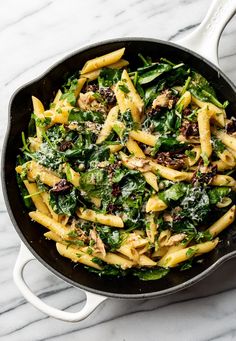 pasta with spinach and chicken in a skillet on a marble countertop, ready to be eaten