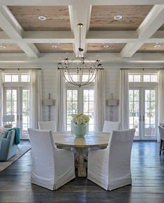 a dining room with white chairs and a chandelier hanging from the wooden ceiling