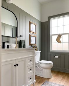 a white toilet sitting next to a window in a bathroom under a framed christmas stocking