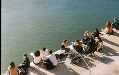 several people sitting on the edge of a body of water with their backs to each other