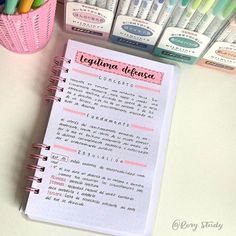 an open notebook with writing on it next to markers and pens in a pink basket