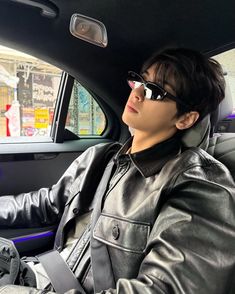 a young man wearing sunglasses sitting in the driver's seat of a car with his hand on the steering wheel