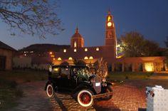 an old fashioned car parked in front of a building with a clock tower at night