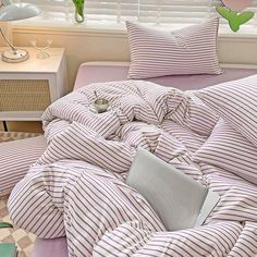 an unmade bed with purple and white striped comforter in a bedroom next to a window