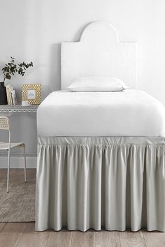 a bed with a white headboard and skirted bedspread in a bedroom