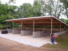 two people are standing in front of a covered area with concrete walls and columns on each side