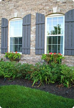 a red fire hydrant sitting in front of a brick building with windows and plants