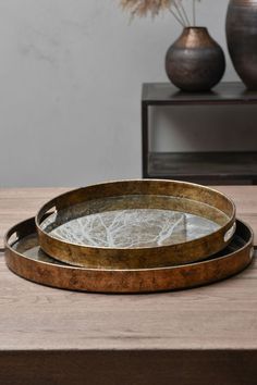 two round metal trays sitting on top of a wooden table next to vases