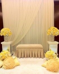 two white vases filled with yellow flowers on top of a table covered in drapes