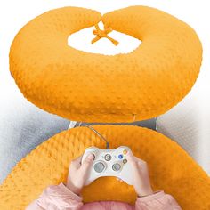 a person is holding a video game controller in front of an orange pillow with a cross on it