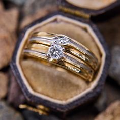 two gold wedding rings sitting on top of each other in a wooden box with rocks