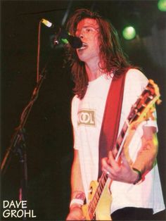 a man with long hair playing guitar in front of a microphone at a music concert