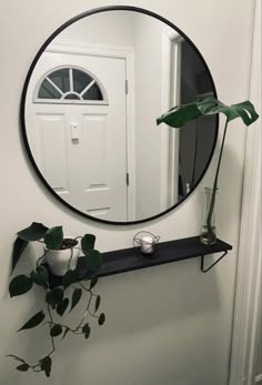 a round mirror hanging on the wall above a shelf with a potted plant next to it