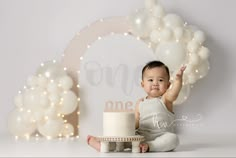 a baby sitting in front of a cake with balloons