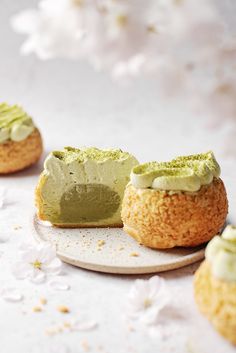 three small pastries with green frosting and flowers in the background on a plate