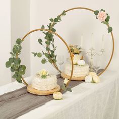 two cakes with flowers and greenery sit on a table