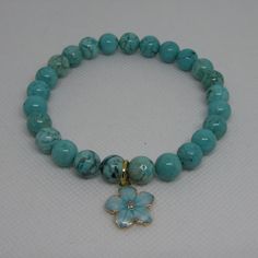 a bracelet with turquoise beads and a gold flower charm on the clasp is sitting on a white surface