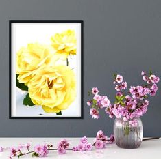 a vase filled with yellow and pink flowers next to a framed photograph on the wall