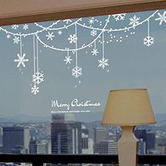 a lamp on a table in front of a window with snowflakes hanging from it