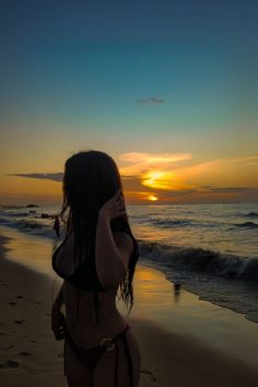 a woman standing on top of a sandy beach next to the ocean at sun set