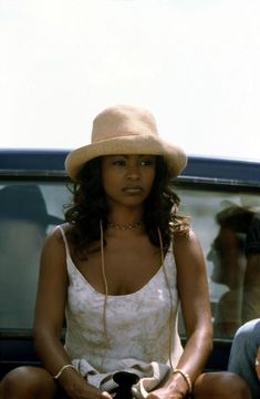 a woman sitting on the back of a car wearing a hat and holding a camera