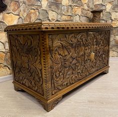 an ornate wooden box sitting on top of a floor next to a stone wall and clock