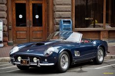 an old blue sports car parked in front of a building with two parking meters attached to it