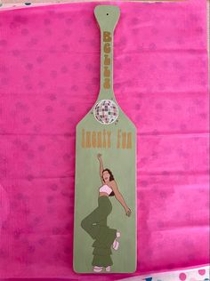 a wooden spoon shaped like a woman with her hand up in the air on a pink background