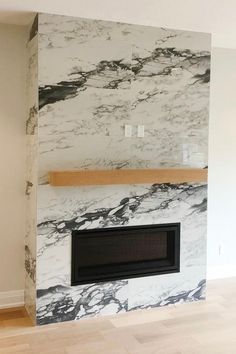 an empty room with a fireplace in the middle and white marble on the back wall