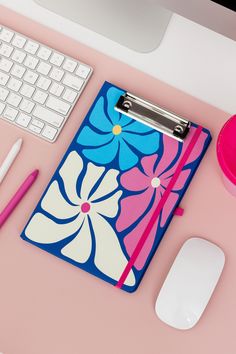 a pink desk with a blue and white flower binder next to a computer keyboard