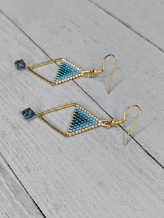 two pairs of gold and blue beaded triangle earrings on white wooden background, closeup