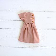 2-3 WEEK TURNAROUND TIME. This dusty rose, light pink cotton/linen handmade dress is the perfect addition to any little's wardrobe! Though great for all year cuteness! Perfect fall and winter with elbow length sleeves. Or summertime fun with the tank version. Dress is a elbow-sleeved or sleeveless, with a lined, slightly curved front bodice. Three wooden button closures in the back of the dress of the 3/4 sleeved version. Tank version has a V-back and 1 button. This fabric is a linen cotton blen Cotton Day Dress With Button Back, Cotton Daywear Dress With Button Back, Pink Buttoned Feminine Dress, Cute Button-up Dress With Buttons, Cute Pink Dresses With Buttons, Feminine Pink Buttoned Dress, Cute Pink Dress With Buttons, Feminine Pink Mini Dress With Buttons, Cute Daywear Dresses With Buttons