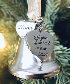 a bell ornament hanging from a christmas tree with the words mom and a piece of my heart is in heaven