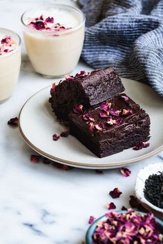 three pieces of brownie on a plate next to two glasses of milk