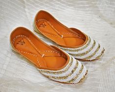 This Embellished Leather Indian Jutti flat is exclusively Handcrafted by specialized craftsmen in India inheriting this craft over generations. The jutti or Punjabi Jutti is a type of footwear common in North India and neighboring regions. They were traditionally made up of leather and with extensive embroidery, in real gold and silver thread as inspired by Indian royalty over 400 years ago. Step up your fashion game with these handmade leather juttis, designed to add a touch of tradition and st Festive Embroidered Leather Flats, Leather Flats For Wedding And Festive Occasions, Traditional White Embroidered Wedding Shoes, Gold Embroidered Wedding Shoes With Round Toe, Gold Embroidered Round Toe Flats, Leather Wedding Flats, White Gota Work Flats With Round Toe, Traditional White Wedding Shoes With Round Toe, Traditional White Flat Wedding Shoes