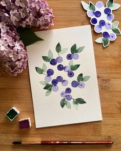 some watercolors are laying on a table next to purple flowers