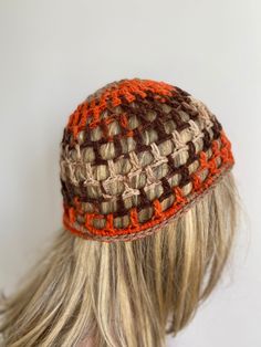 a woman with long blonde hair wearing a brown and orange crochet beanie