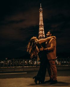 a man and woman dancing in front of the eiffel tower at night with their arms around each other