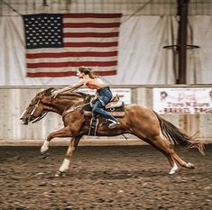 a woman riding on the back of a brown horse in front of an american flag