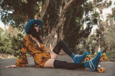 a woman sitting on the ground with her legs crossed wearing roller skates and a blue hat