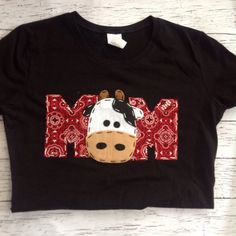 a black t - shirt with a cow on it's chest and the word mom written in red