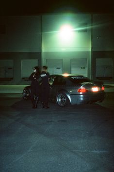 two police officers standing in front of their cars at night, talking to each other